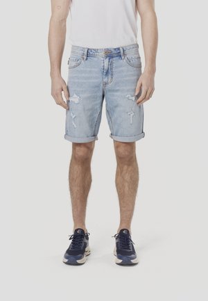 Jeansshorts in Hellblau mit Used-Optik und umgeschlagenen Säumen. Kombiniert mit marineblauen Sportschuhen. Schlichtes Design und lässige Passform.
