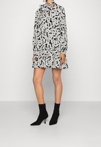Vestido negro con estampados abstractos en blanco, mangas largas y dobladillo acampanado. Combinado con botines de ante negros con puntas afiladas.