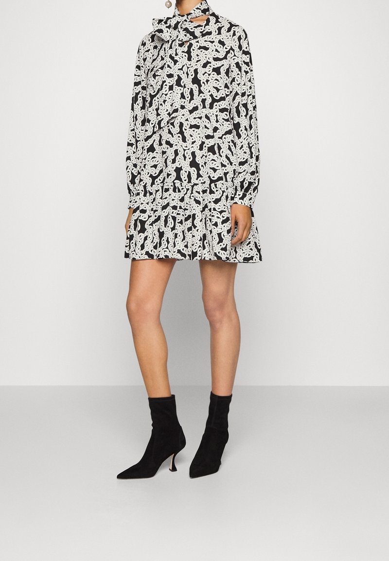 Vestido negro con estampados abstractos en blanco, mangas largas y dobladillo acampanado. Combinado con botines de ante negros con puntas afiladas.