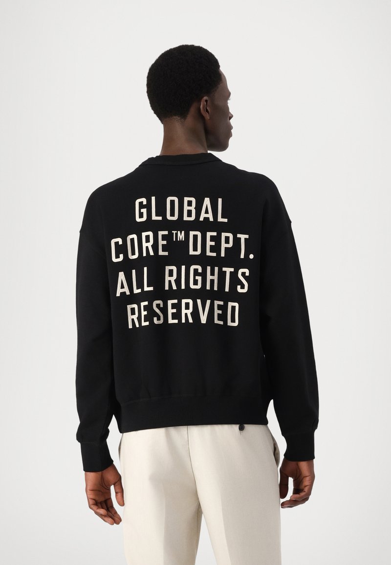 Czarna bluza z białym napisem z tyłu, brzmiącym "GLOBAL CORE™ DEPT. WSZYSTKIE PRAWA ZASTRZEŻONE." Żebrowane mankiety i dół. Miękka textura materiału.