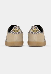 Beige Sneakers mit einem Leopardenmuster hinten, goldfarbenem Logo-Detail und strukturiertem Gummisohle. Weiches Wildledermaterial mit einem flachen Design.