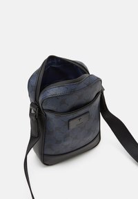 Borsa blu navy con motivo testurizzato, chiusura con zip, dettagli neri, tracolla regolabile e placca con logo nella parte frontale. L'interno è foderato in blu navy.