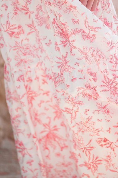 Vestido branco com um delicado padrão floral em vermelho, apresentando um design fluido e tecido suave. Notável barra em babados e detalhes intrincados.