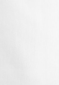 Fond en tissu blanc texturé uni avec motif tissé visible et variations subtiles d’éclairage.