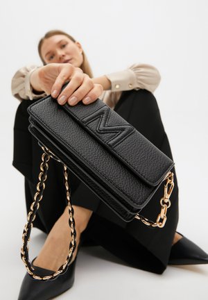 Borsa a tracolla in pelle nera con textura, dotata di una chiusura a patta magnetica e di un logo "M" impresso in evidenza.