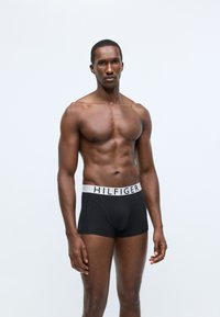 Fekete boxeralsó, fehér elasztikus derékpánttal, amelyen a "HILFIGER" logó található. Kényelmes, testhezálló fazonban készült, puha, rugalmas anyagból.