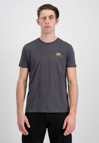 Grå t-shirt med kort ærme lavet af bomuld, der har en rund hals, et lille neongrønt logo på brystet og flade sømme.
