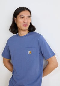 T-shirt in cotone blu con maniche corte, scollo rotondo e tasca sul petto con patch logo. Texture liscia e vestibilità comoda.