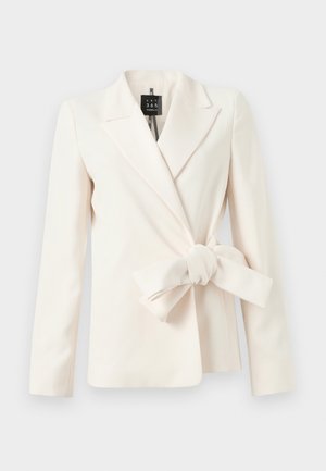 Kremfarget tilpasset blazer med lange ermer og en stor stoffsløyfe knyttet i midjen på en ensfarget bakgrunn.