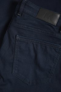 Granatowe dżinsy z denimu z skórzaną metką, detalami na tylnej kieszeni oraz kontrastowym przeszyciem. Gładka tekstura, klasyczny krój.