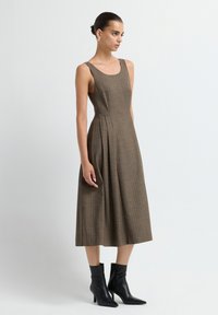 Vestido sin mangas de cuadros marrones con un torso ajustado y falda acampanada, combinado con botines negros. Textura suave, con sutiles pliegues en la cintura.