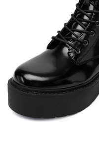 Czarne lakierowane botki na wysokim obcasie z błyszczącym wykończeniem, okrągłym noskiem, grubą czarną platformą i czarnymi sznurowaniami.