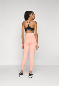 Black sports bra with thin straps and logo detail, paired with high-waisted, light pink leggings, and black athletic shoes.