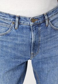 Jeans de denim azul con un diseño clásico, que cuentan con un cierre de botón de metal, un ligero desgastado y costuras en contraste a lo largo de las costuras.