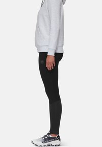 Felpa grigia con tasca frontale, abbinata a leggings neri con logo. Scarpe da ginnastica in bianco e nero completano l'outfit.