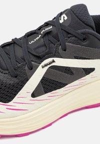 Svart löparsko med vit och rosa sula, ovandel i mesh, svarta snören och "ULTRA FLOW" tryckt nära tungan.