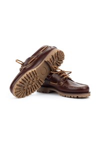 Zapatos de barco de cuero marrón con una suela de goma robusta en tono beige, que presentan un diseño con cordones, un detallado de costura y ojales de metal.