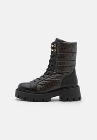 Bottes de combat en cuir noir avec un côté à motif marron, accents en métal doré, semelle épaisse et col rembourré.