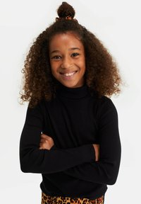 Fekete bordás garbós pulóver hosszú ujjakkal, leopárdmintás alsóval párosítva. A modellen göndör haj van, amelyet kontyba kötött.