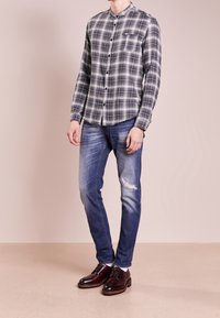 Károvaná košile na knoflíky v černé a šedé barvě, doplněná o potrhané modré džíny a hnědé kožené šněrovací boty. Hladká textura a volný střih.