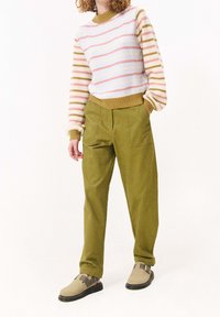 Pletený svetr v bílých, růžových a olivových pruzích; v kombinaci s olivově zelenými kalhotami s širokými nohavicemi a béžovými dřeváky s tmavými podrážkami a přezkami.