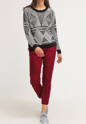 Pull rayé noir et blanc avec des motifs géométriques, associé à un pantalon bordeaux et des baskets grises. Coupe décontractée, bords côtes.