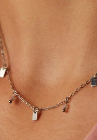 Zilveren ketting met rechthoekige hangers en kleine bolvormige accenten. Het ontwerp bevat schakels en gestructureerde oppervlakken.