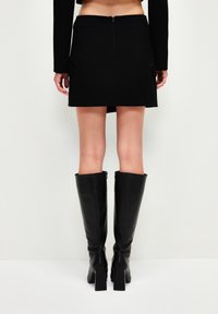Mini falda negra con un diseño ajustado, que presenta un cierre de cremallera en la parte posterior. Estilizada con botas de cuero negro hasta la rodilla y una blusa corta.