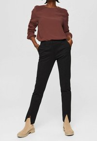 Blusa bordeaux con dettagli plissettati sulle spalle abbinata a pantaloni neri su misura con spacco laterale, completata da stivaletti beige alla caviglia.