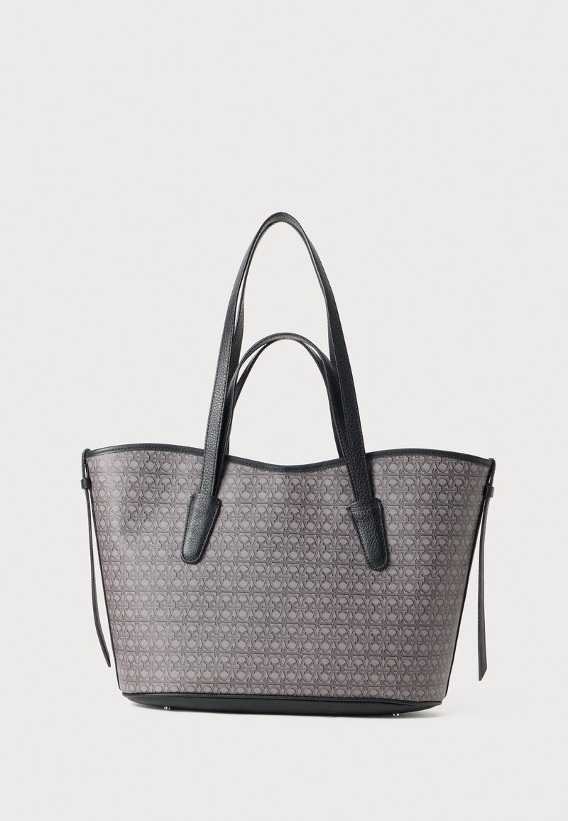 Sac fourre-tout en tissu gris à motifs avec des accents en cuir noir. Présente deux longues poignées et un détail zippé sur le côté.