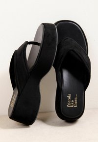 Sandales compensées noires avec des brides épaisses, l'une reposant sur le côté et l'autre en position verticale, avec un texte doré « friends like these… » sur la semelle intérieure.