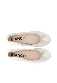 Ballerine in suede crema con punta arrotondata e un piccolo fiocco sul davanti. La soletta interna presenta la scritta "BIANCO" in lettere nere.