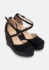 Tacchi a cuneo neri con una base in espadrille intrecciata texturizzata, presentano una tomaia in suede e cinghie incrociate alla caviglia per una vestibilità sicura. Design con punta arrotondata.