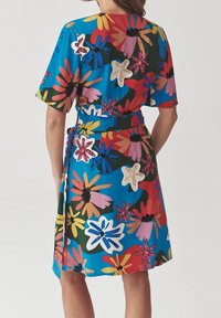 Lyhythihainen mekko, jossa on kirkas sininen väri ja suuret kukkakuviot vaaleanpunaisena, keltaisena ja punaisena. Mekossa on solmittava vyötärö ja rento istuvuus.