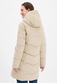 Doudoune beige avec un tissu texturé à rayures, motif en chevron et capuche. Elle présente un poignet boutonné et un design mi-long.