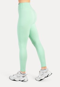 Mintgröna leggings med hög midja, gjorda av mjukt, stretchigt tyg. Bärs med vita och silvriga träningsskor.