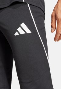 Schwarze Sporthose aus glattem, elastischem Stoff mit einem weißen seitlichen Streifen und einem auffälligen weißen Adidas-Logo.