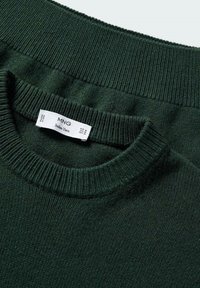 Pull en maille vert foncé avec col rond côtelé, montrant une étiquette de vêtement blanche indiquant "MNG Italian Yarn" et taille moyenne.