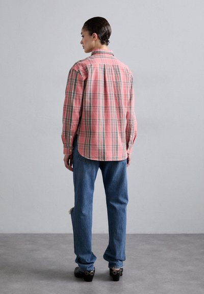 Camisa de cuadros roja y gris con cuello abotonado, combinada con jeans azules desgastados y zapatos de tacón negros. Detalles de costura visibles.