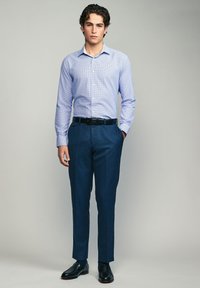 Chemise boutonnée à motif bleu clair associée à un pantalon de costume bleu foncé et des chaussures noires. La chemise présente un col standard et des manches longues.