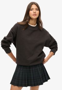 Mørkegrå oversized sweatshirt med ribbede, manchetterede ærmer, parret med en plisseret sort og grønternet nederdel. Casual, behageligt design.