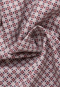 Tessuto intrecciato con una superficie texture, caratterizzato da un motivo geometrico in rosso, beige e nero, disposto in un design a griglia.