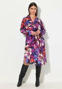 Sukienka w kwiatowy wzór z kołnierzykiem, w intensywnych odcieniach fioletu, różu i czerwieni. Długie rękawy, zwiewny fason, rozcięcia sięgające ud.