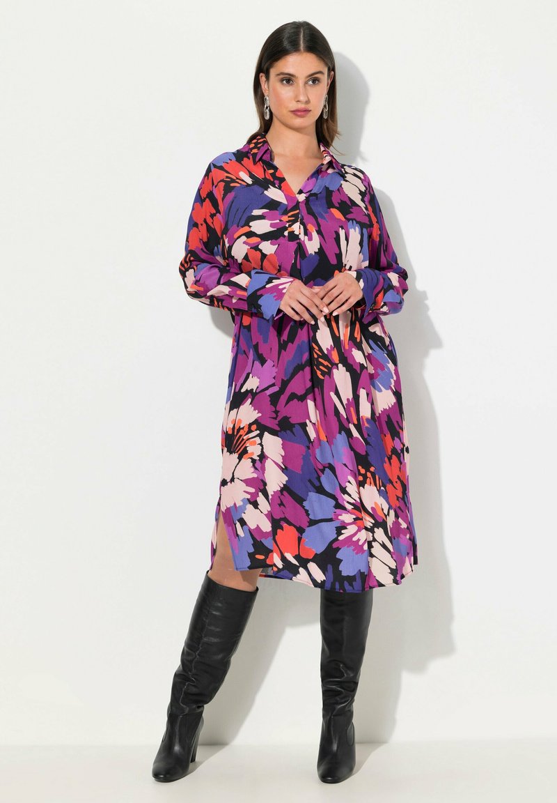 Sukienka w kwiatowy wzór z kołnierzykiem, w intensywnych odcieniach fioletu, różu i czerwieni. Długie rękawy, zwiewny fason, rozcięcia sięgające ud.
