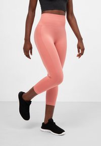 Leggings a vita alta, a coste e cropped di un morbido colore corallo, abbinati a scarpe da ginnastica nere, con una comoda cintura elastica.