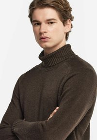 Brun polotröja med ribbad krage och långa ärmar. Tyget verkar mjukt med en slät yta och en figurnära silhuett.