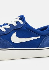 Blue canvas sneaker featuring a white leather Swoosh, white laces, and a contrasting black sole. Soft texture with suede accents.