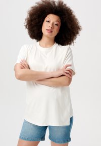 Hvid kortærmet t-shirt lavet af bomuld, med rund hals. Kombineret med denim shorts, der viser en afslappet pasform og casual stil.