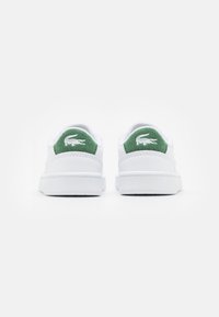 Sneakers bianchi con dettagli in feltro verde sul tallone, dotati di un logo. Il design presenta un esterno in pelle liscia e una suola in gomma.