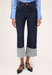 Pantaloni scurți din denim închis, cu tivuri deschise din denim franjurat și cusături contrastante. Prezintă buzunare frontale și un sistem de închidere cu nasturi.